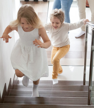 Two kids running up some stairs inside a house